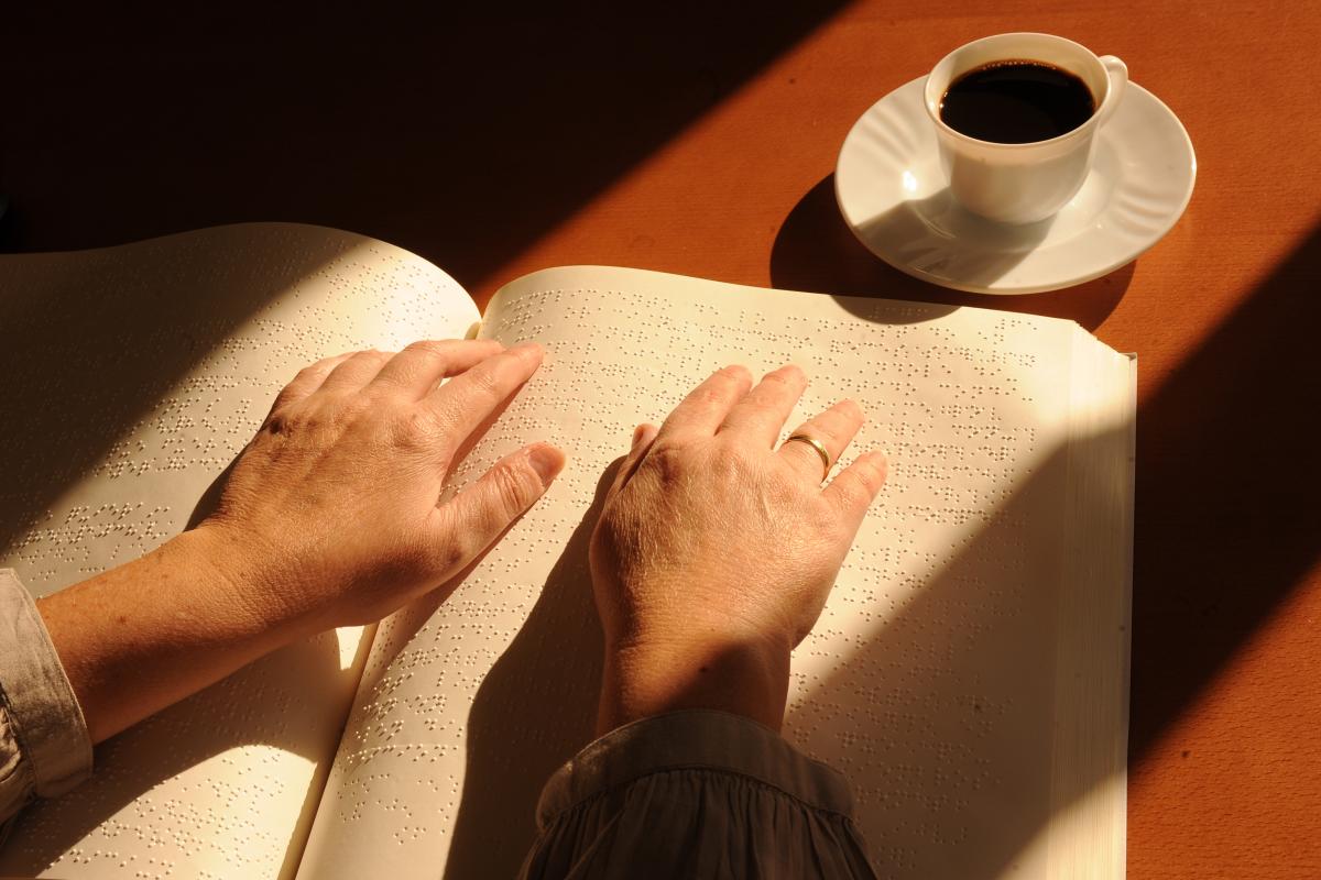 En la imagen, los dedos  de una persona se deslizan por una página de un libro escrito en braille