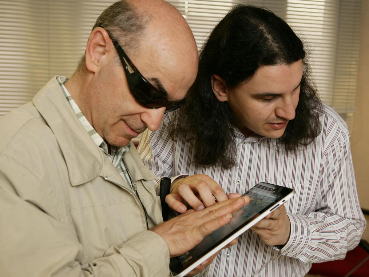 Imagen de  un técnico de ONCE  ayudando  a un afiliado a manejar una tablet