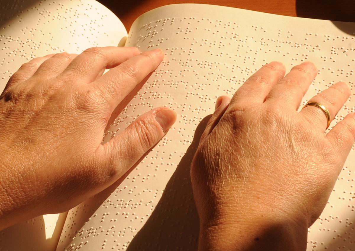 Imagen de los dedos de  una mano posada sobre la página de un libro en braille