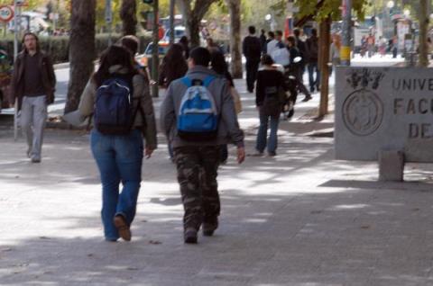 Estudiantes caminan con sus mochilas a la espalda hacia una Facultad de un campus universitario