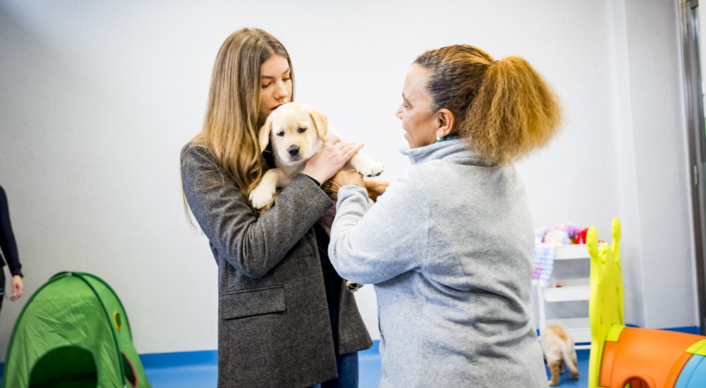 La Infanta Sofía con un cachorro de futuro perro guía en brazos junto a una educadora