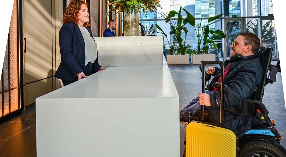 Un cliente usuario de silla de ruedas es atendido en un mostrador accesible en la recepción de un hotel ILUNION