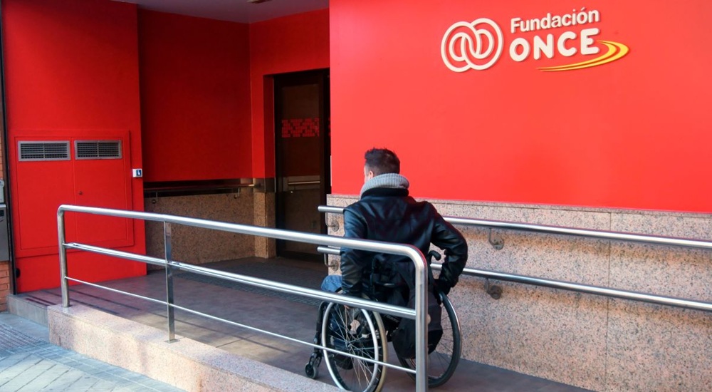 Una persona en silla de ruedas accediendo por la rampa de entrada al edificio de Fundación ONCE en Madrid