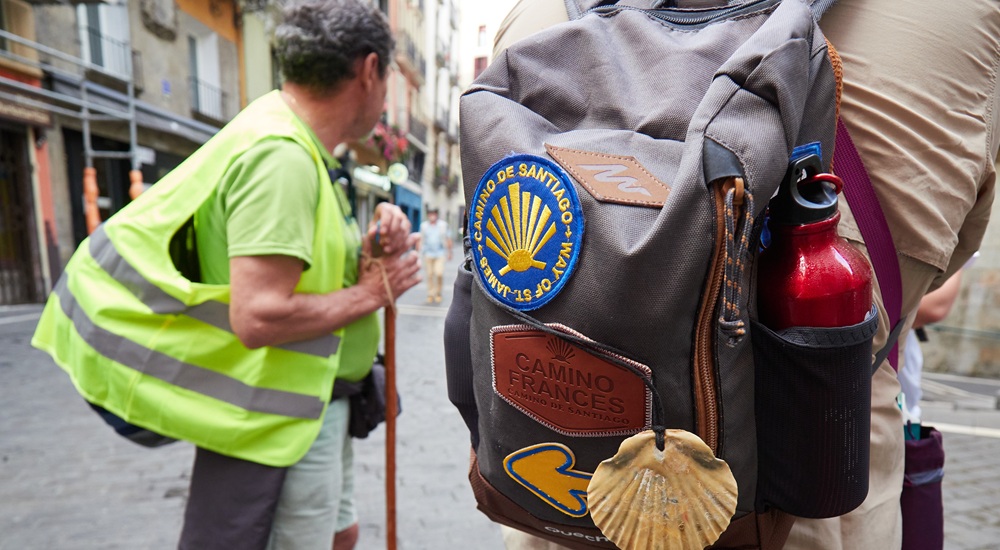 Dos peregrino, uno lleva una mochila con pegatinas del Camino de Santiago