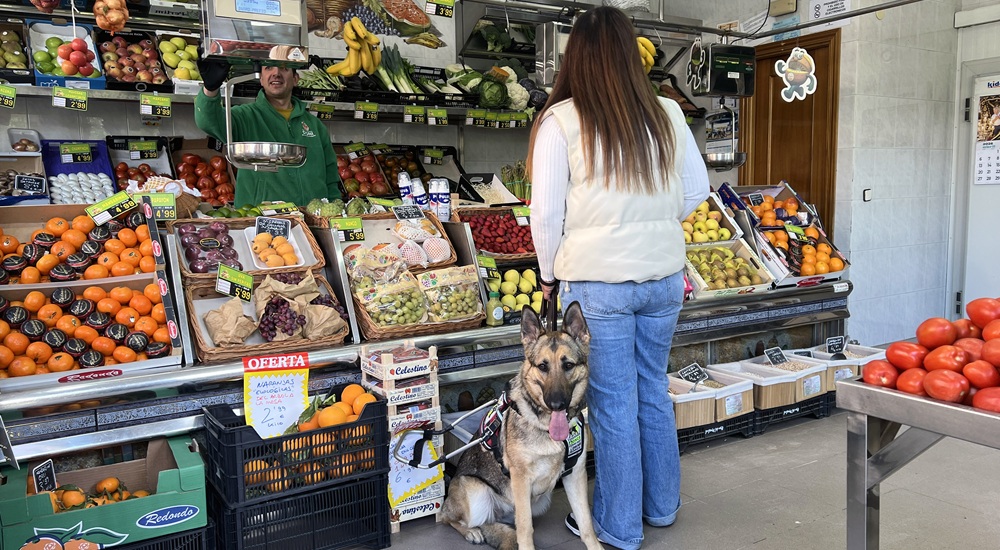 Una usuaria junto a su perro guía en una frutería
