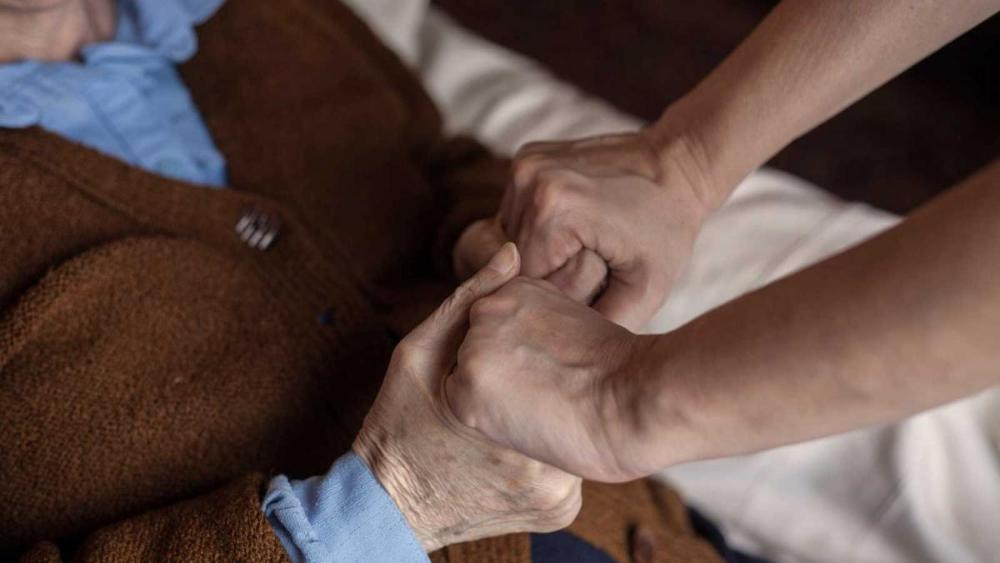 Unas manos adultas sujetan firmemente unas manos ancianas