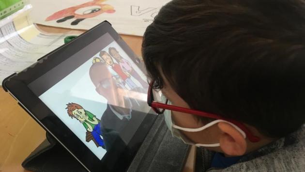 Un niño con discapacidad visual y con mascarilla quirúrgica, sigue una clase telemática a través d e Internet