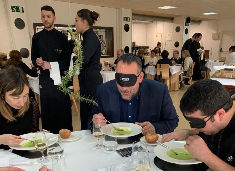 Una vista  del comedor durante el almuerzo con dos alumnos  afiliados deguntando el menú , en primer plano, y detrás de ellos, dos alumnos del servicios de camareros pendientes del desarrollo