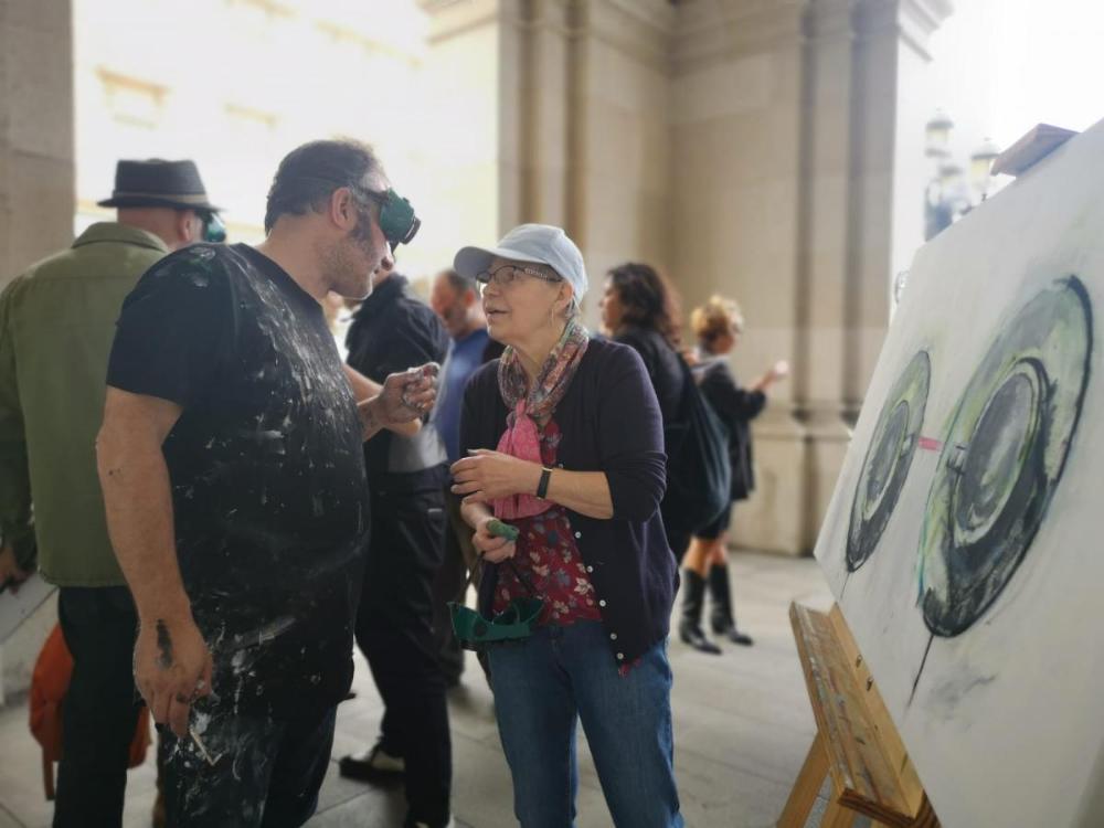 En la imagen aparece en primer término Evelyne de Vos hablando con uno de los artistas participantes en la experiencia