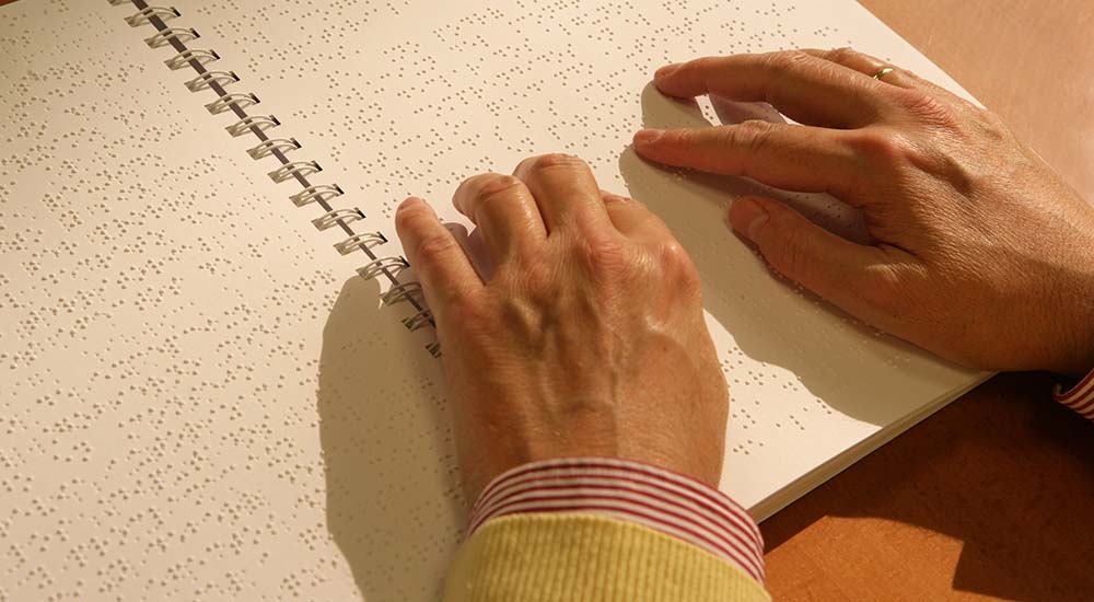 Las manos de una persona ciega leyendo un libro en braille